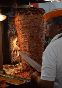 Al pastor meat cooking on spit in front of fire. Man with knife ready to carve meat