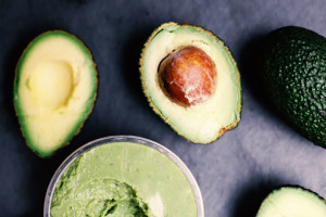 Top-down view of an avocado sliced in half on grey background. Bowl of guacamole nearby.